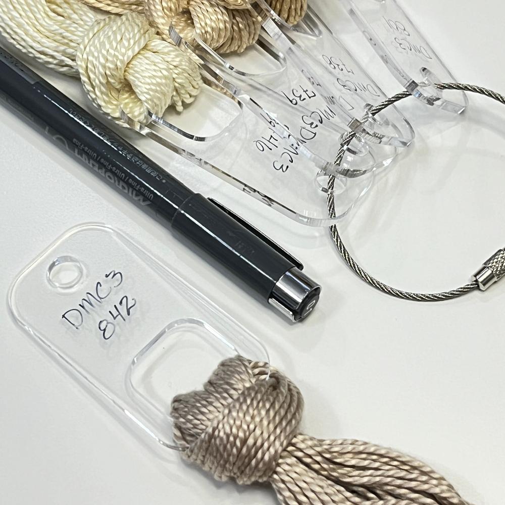 One fiber drop with a light brown perle cotton in the foreground with a marking pen and four more fiber drops with various shades of brown perle cotton on a cable ring