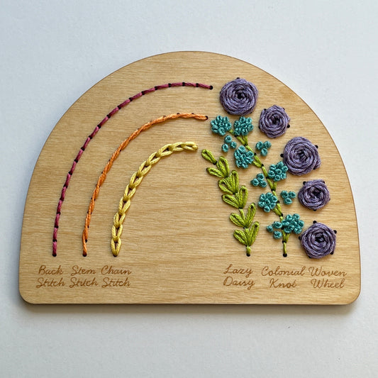 Wooden Laser cut plate in a half circle shape stitched with a colorful rainbow of floss illustrating six different labeled stitches