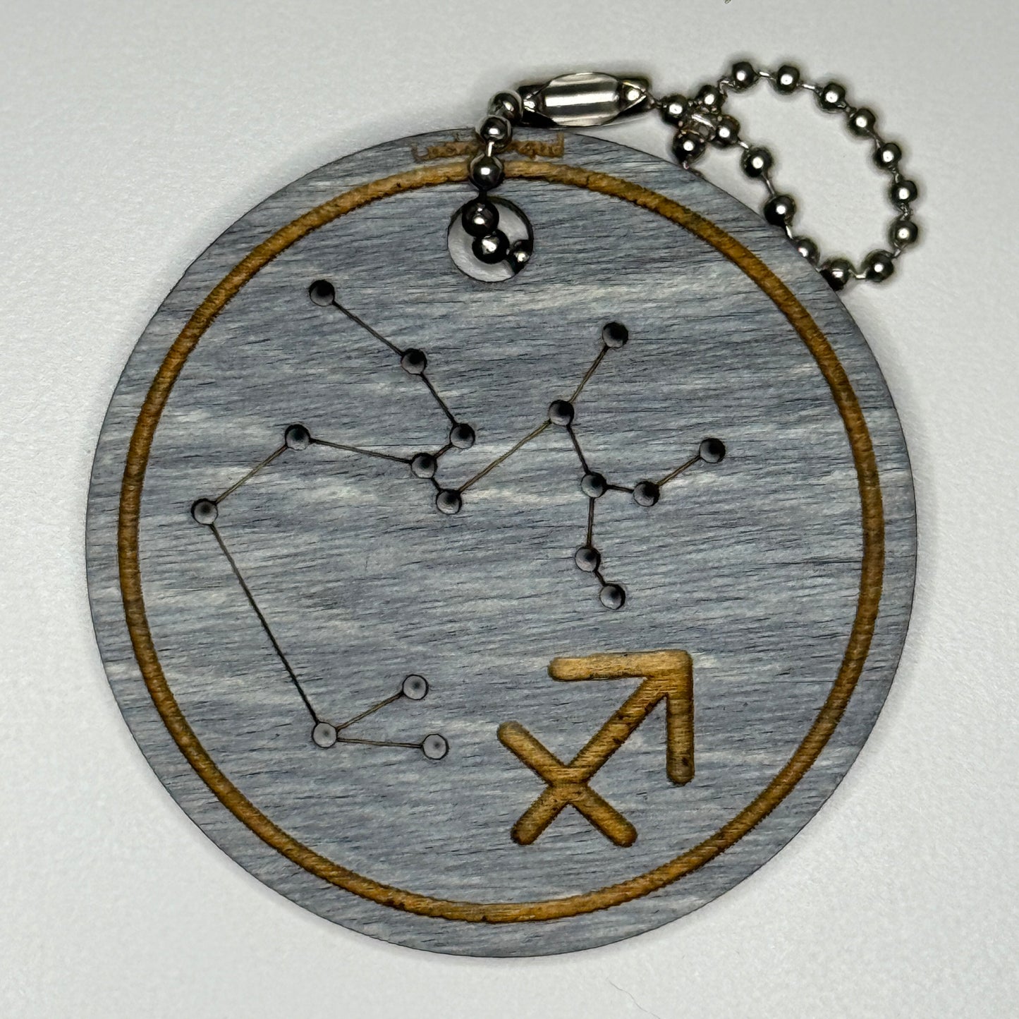 Circular pendant with astrological symbol & stars on a blue wood, set against a white background